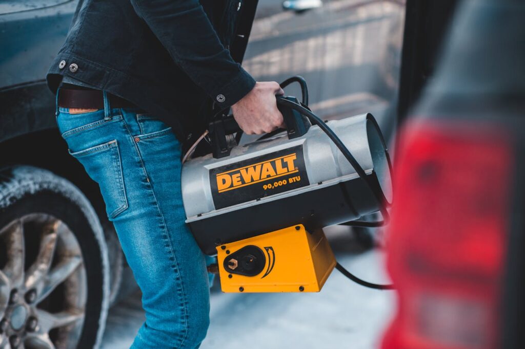 A person carrying a DeWalt portable heater during winter with frosted cars nearby.